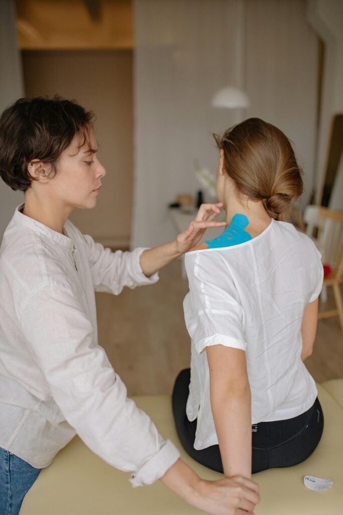 Home A chiropractor applying therapy tape during a shoulder treatment session indoors.